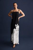 Woman wearing a black slip dress with white floral embroidery on a dark blue background