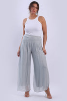 Woman wearing a white tank top and light gray wide-leg pants on a white background