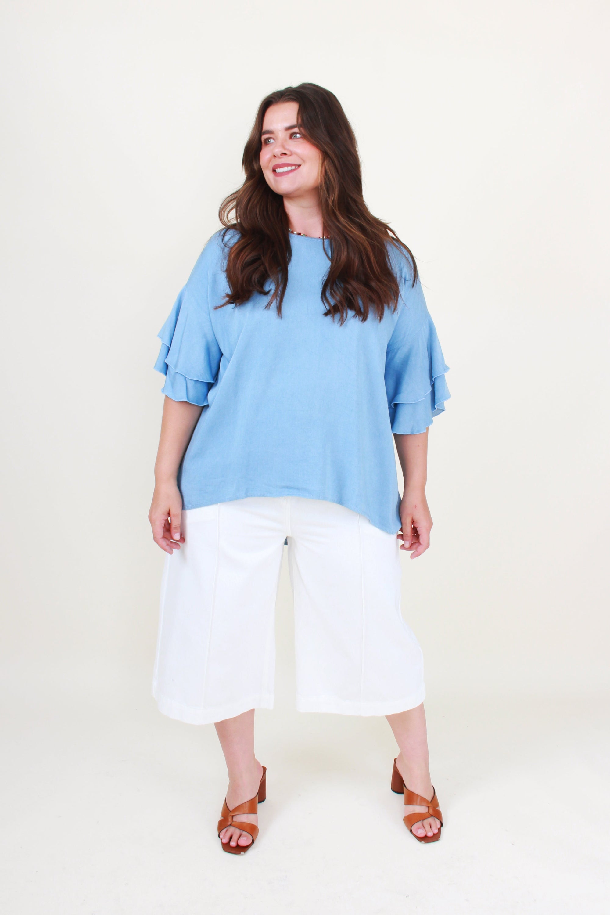 Woman wearing a blue top and white pants on a plain background