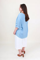 Woman wearing a light blue top and white pants on a plain background