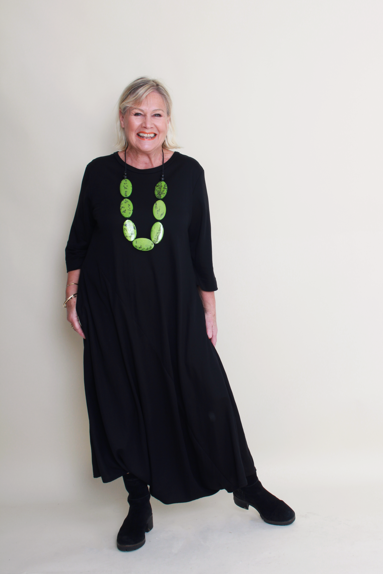 Woman wearing a black dress with green necklace against a white background