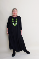 Woman wearing a black dress with green necklace against a white background