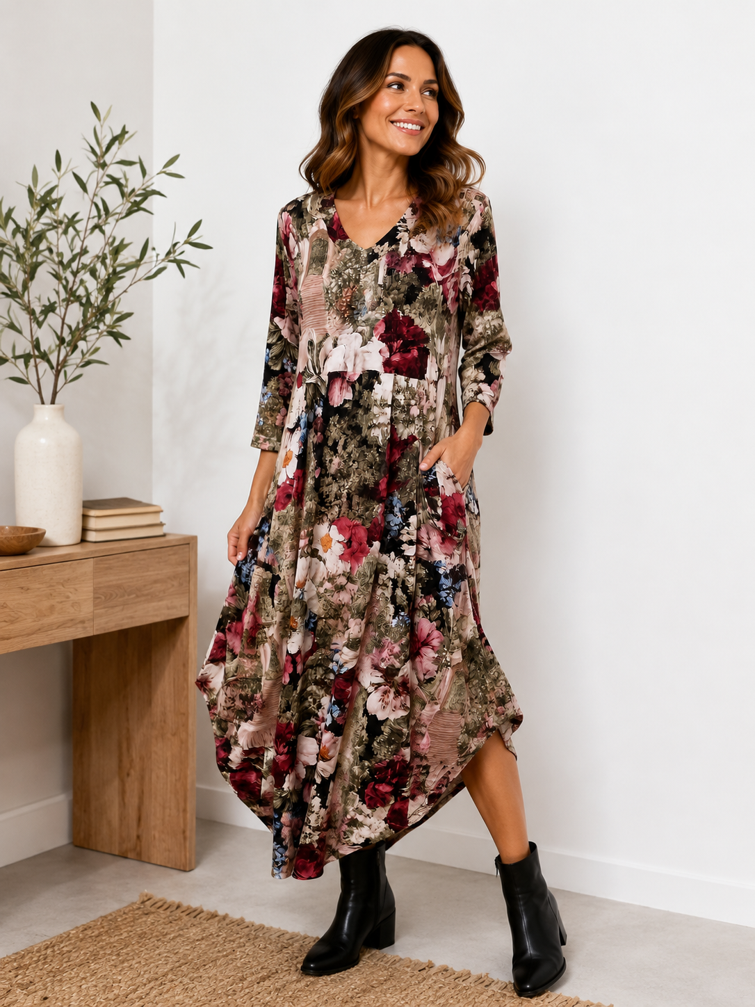 Woman wearing a floral dress standing in a room with a wooden table and plant.