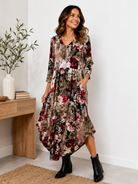 Woman wearing a floral dress standing in a room with a wooden table and plant.