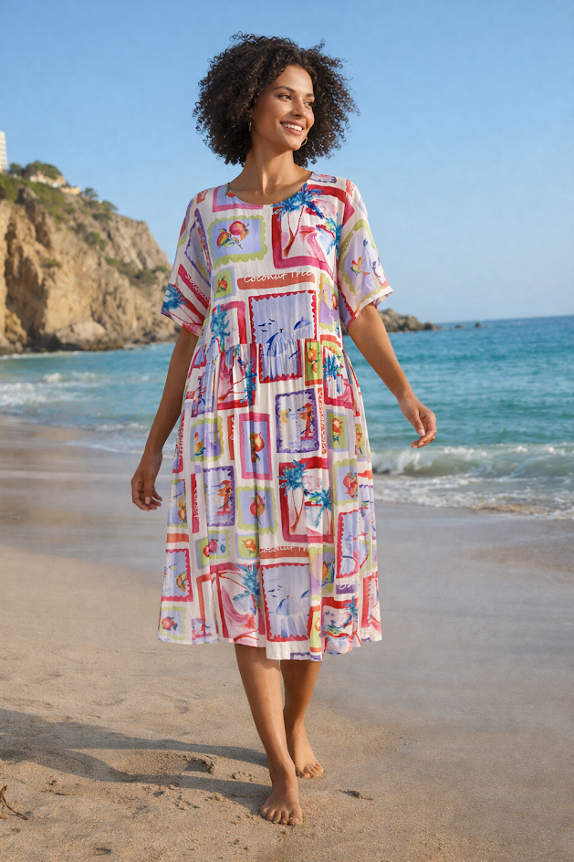 A woman walking barefoot on a sandy beach wearing a short-sleeve, knee-length dress with a colorful patchwork print featuring red, blue, yellow, and white panels.