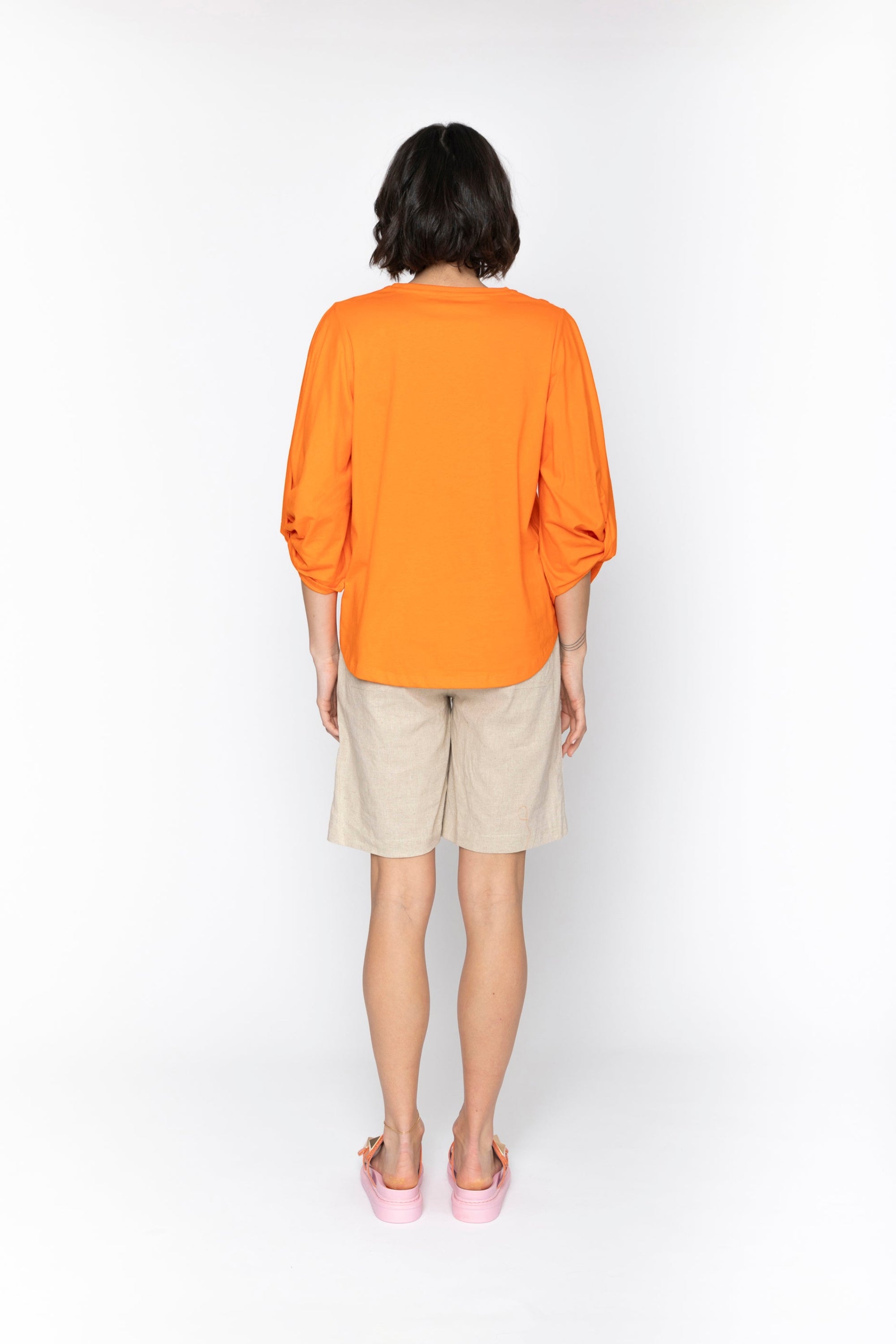 Person wearing an orange shirt and beige shorts on a white background