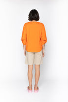 Person wearing an orange shirt and beige shorts on a white background