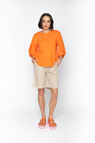 Woman wearing an orange top and beige shorts on a white background
