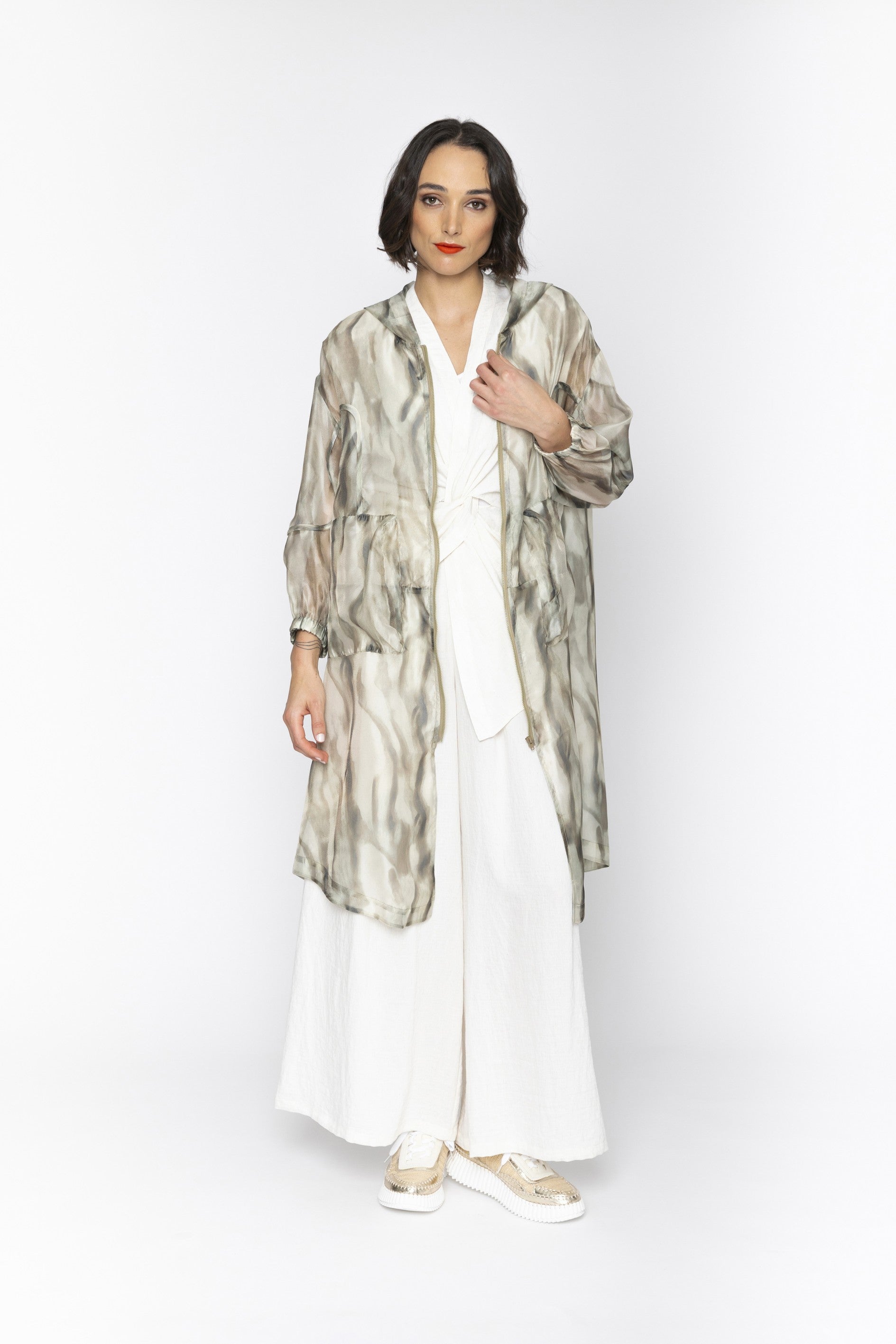 Woman wearing a long, patterned jacket over a white outfit on a white background