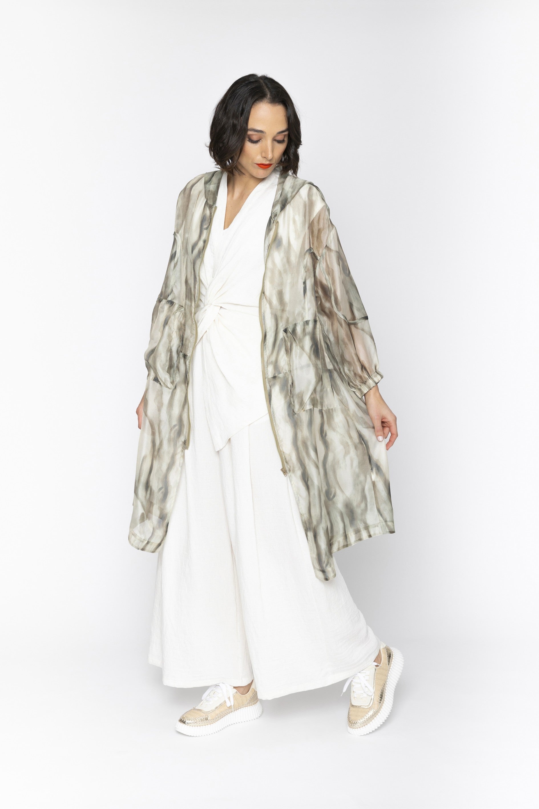 Woman wearing a white outfit with a sheer patterned jacket on a white background