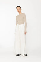 Person wearing a beige sweater and white pants on a white background