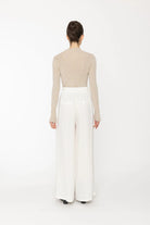 Person wearing a beige long-sleeve top and white wide-leg pants on a white background back angle