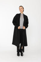 Person wearing a black coat over a gray sweater on a white background