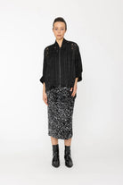 Person wearing a black patterned jacket and skirt on a white background