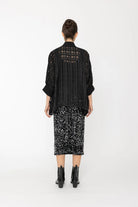 Person wearing a black outfit with sheer details on a white background back angle