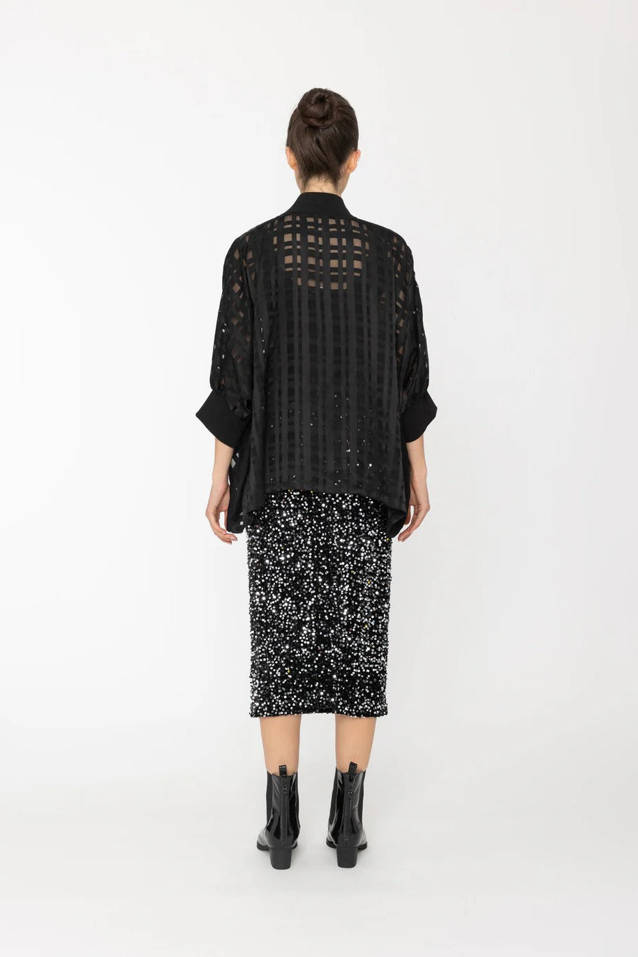Person wearing a black outfit with sheer details on a white background back angle