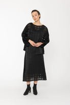 Woman wearing a black outfit with a textured top and skirt on a white background