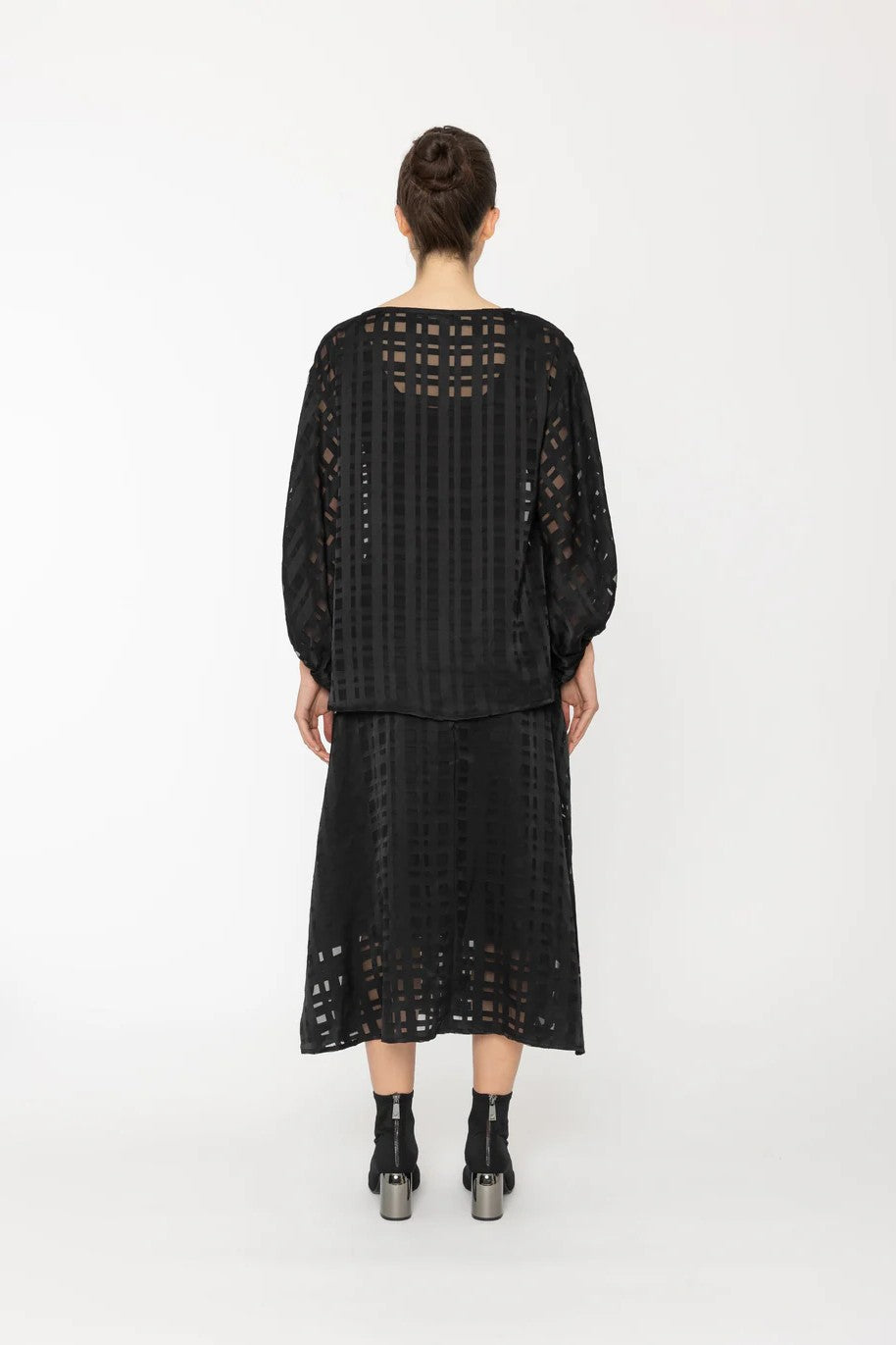 Person wearing a black outfit with lace details on a white background back angle