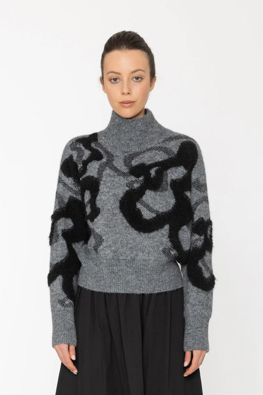 Woman wearing a gray sweater with black abstract patterns on a white background