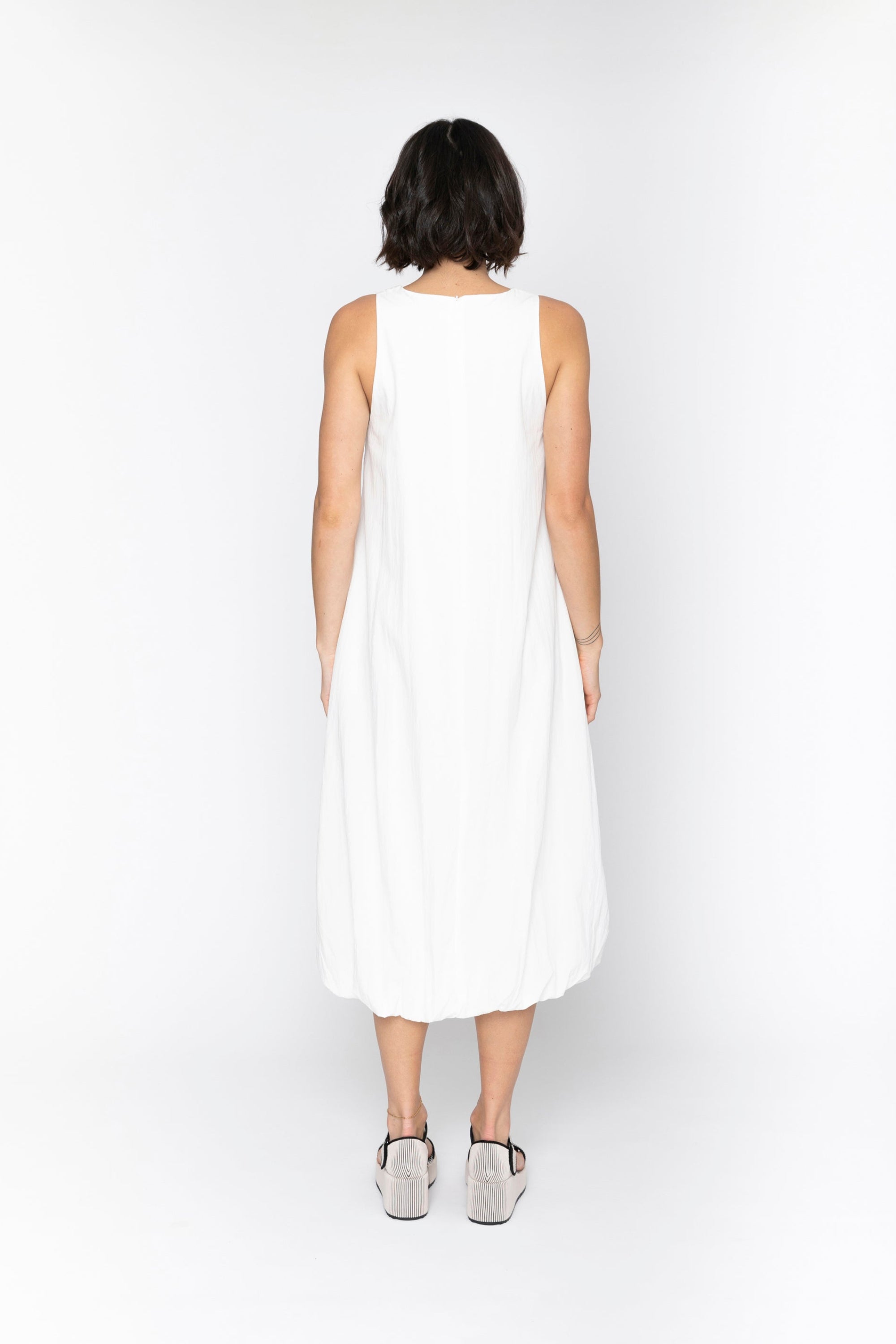 Person wearing a white sleeveless dress on a white background back
