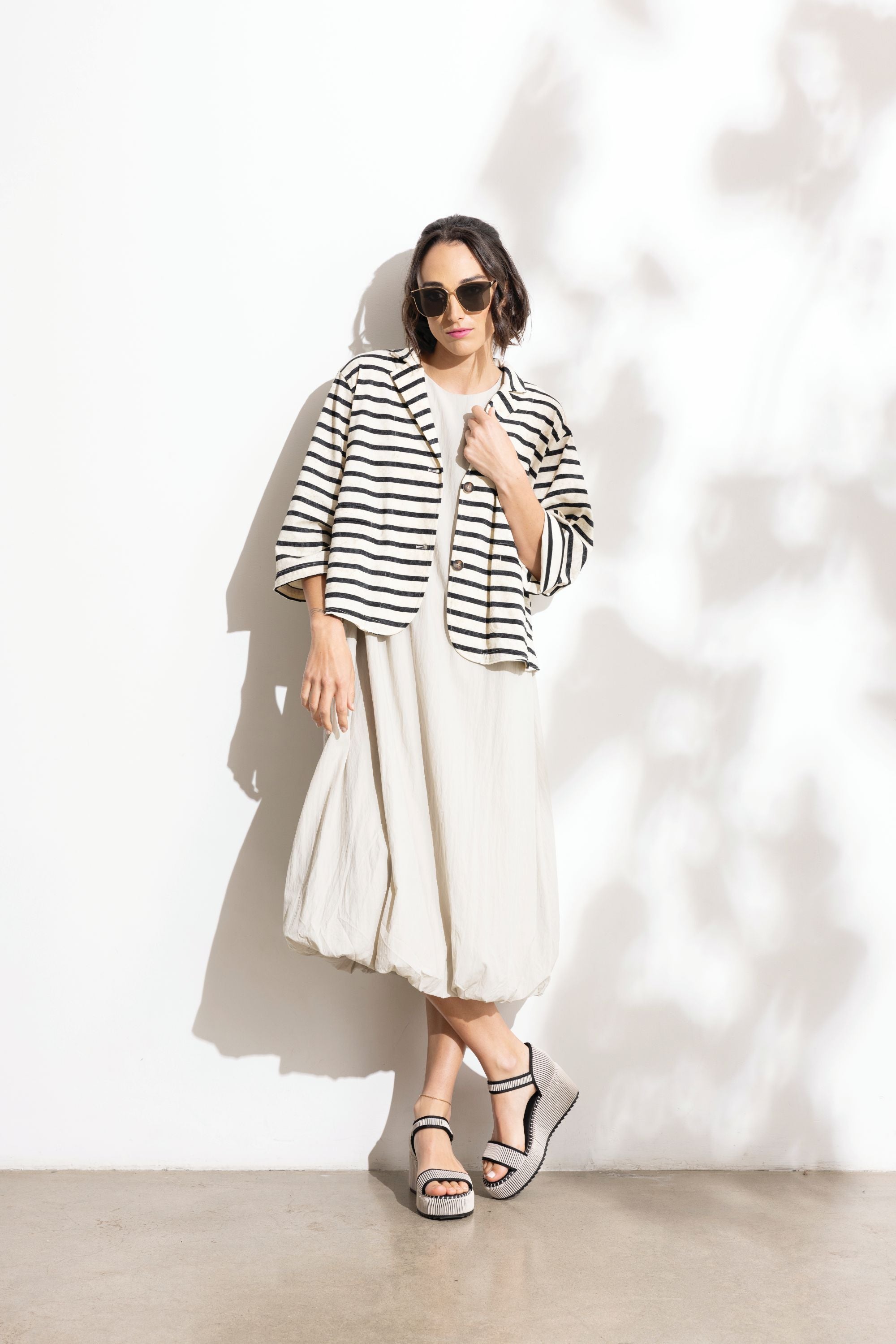 Woman wearing a black and white striped jacket with a white skirt against a white background