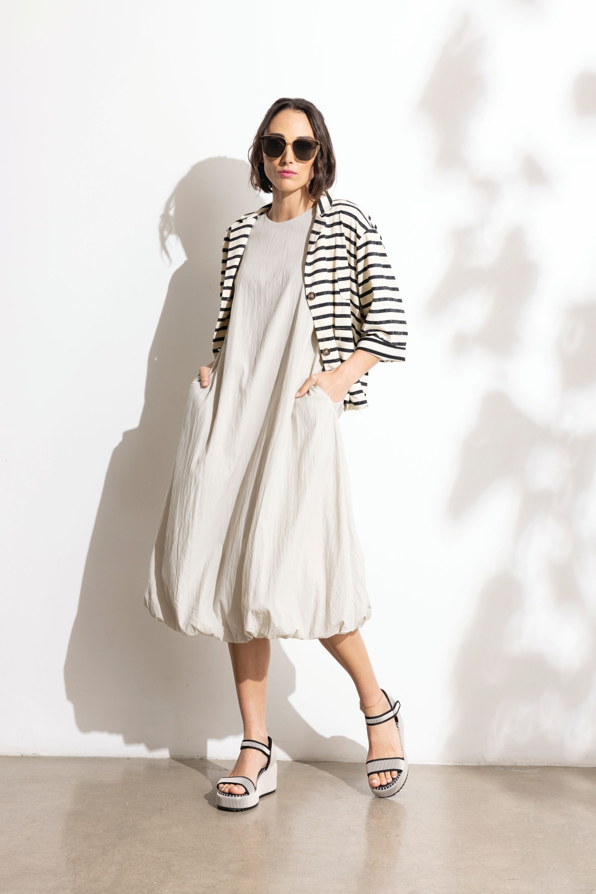 Woman wearing a striped jacket over a long dress with sunglasses against a white background