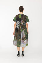 Woman wearing a green abstract patterned dress on a white background back angle