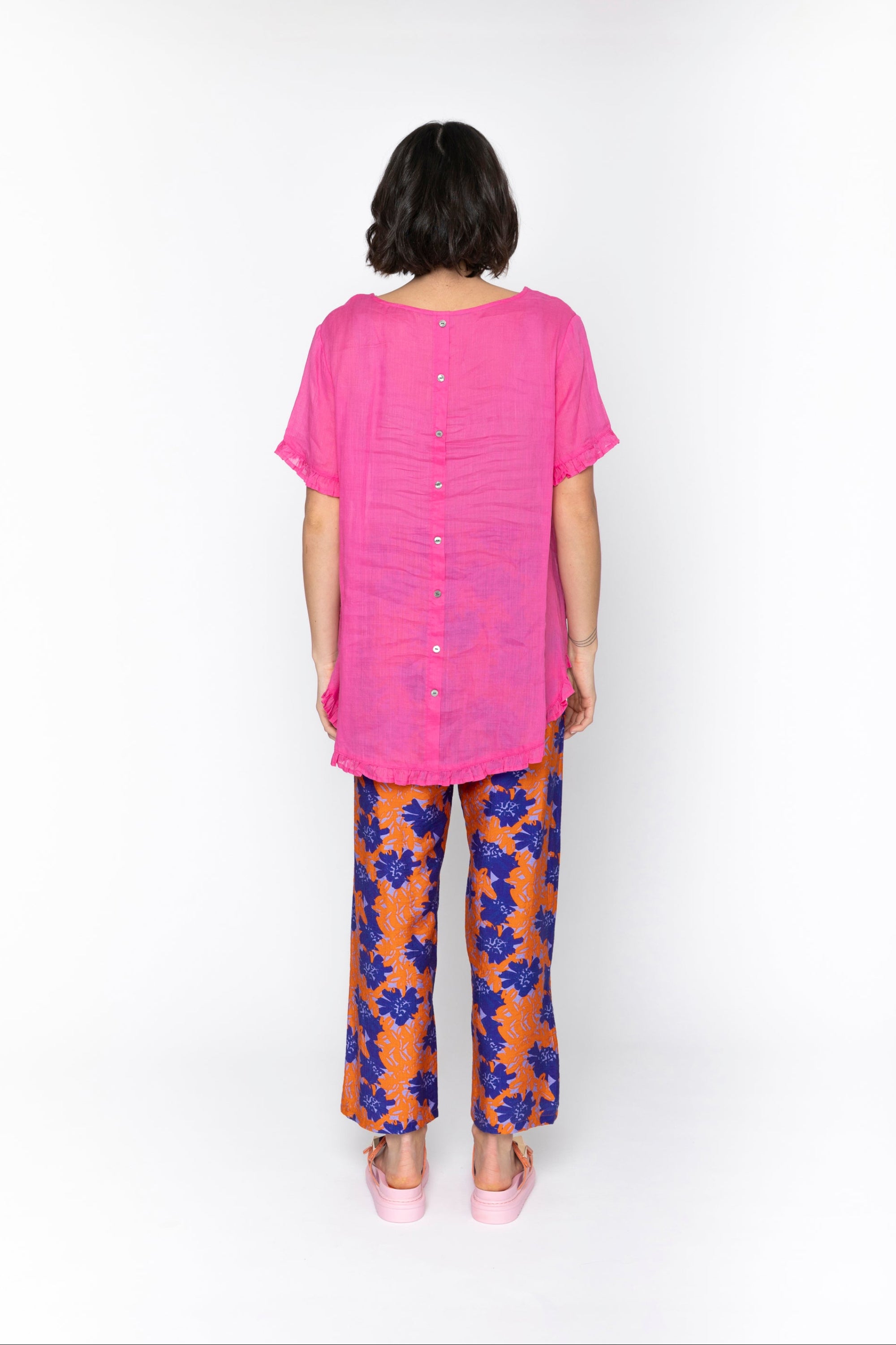Person wearing a pink top and floral pants on a white background back