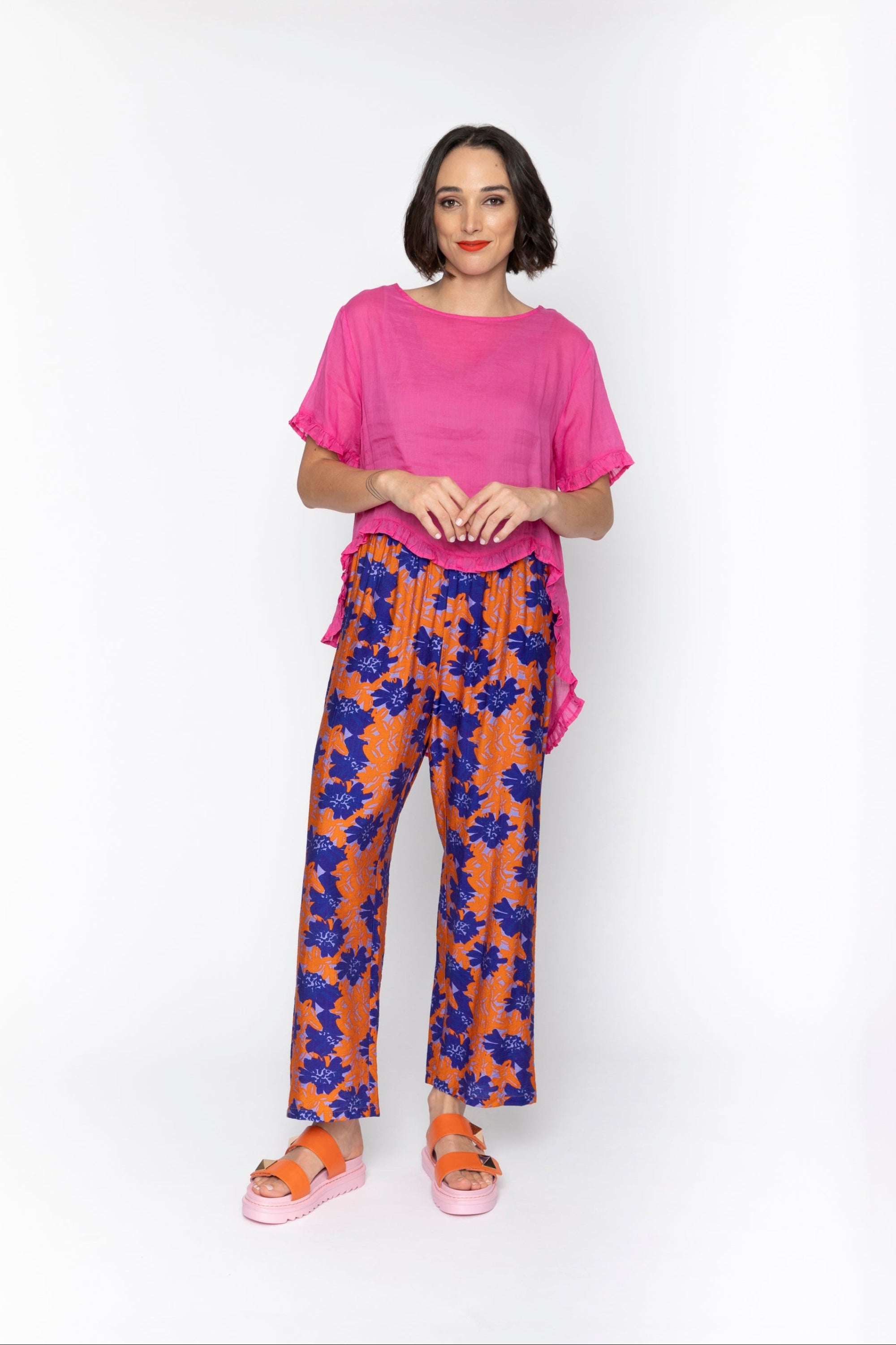 Woman wearing a pink top and floral pants on a white background