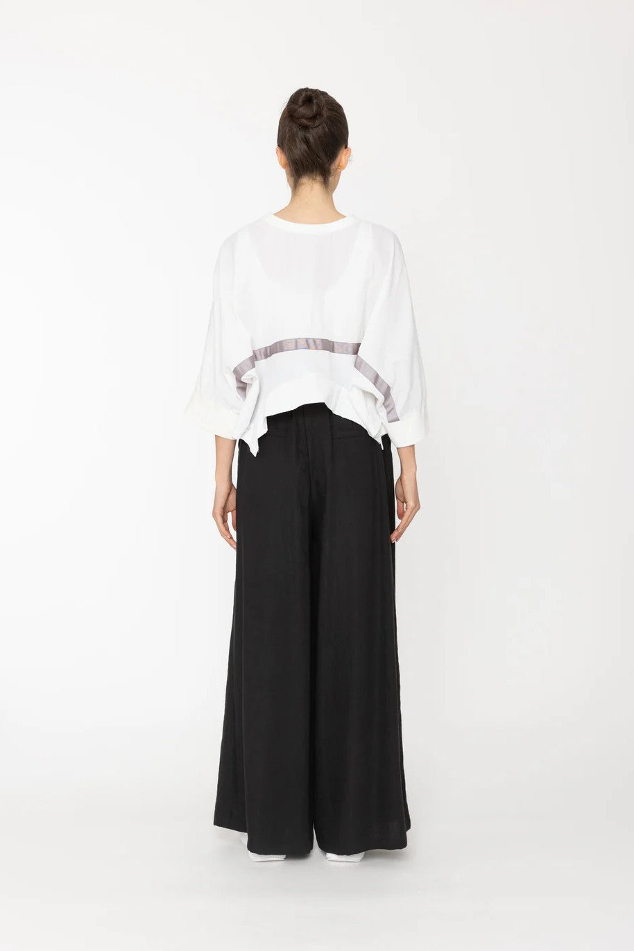 Person wearing a white top and black pants on a white background back angle
