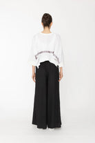 Person wearing a white top and black pants on a white background back angle