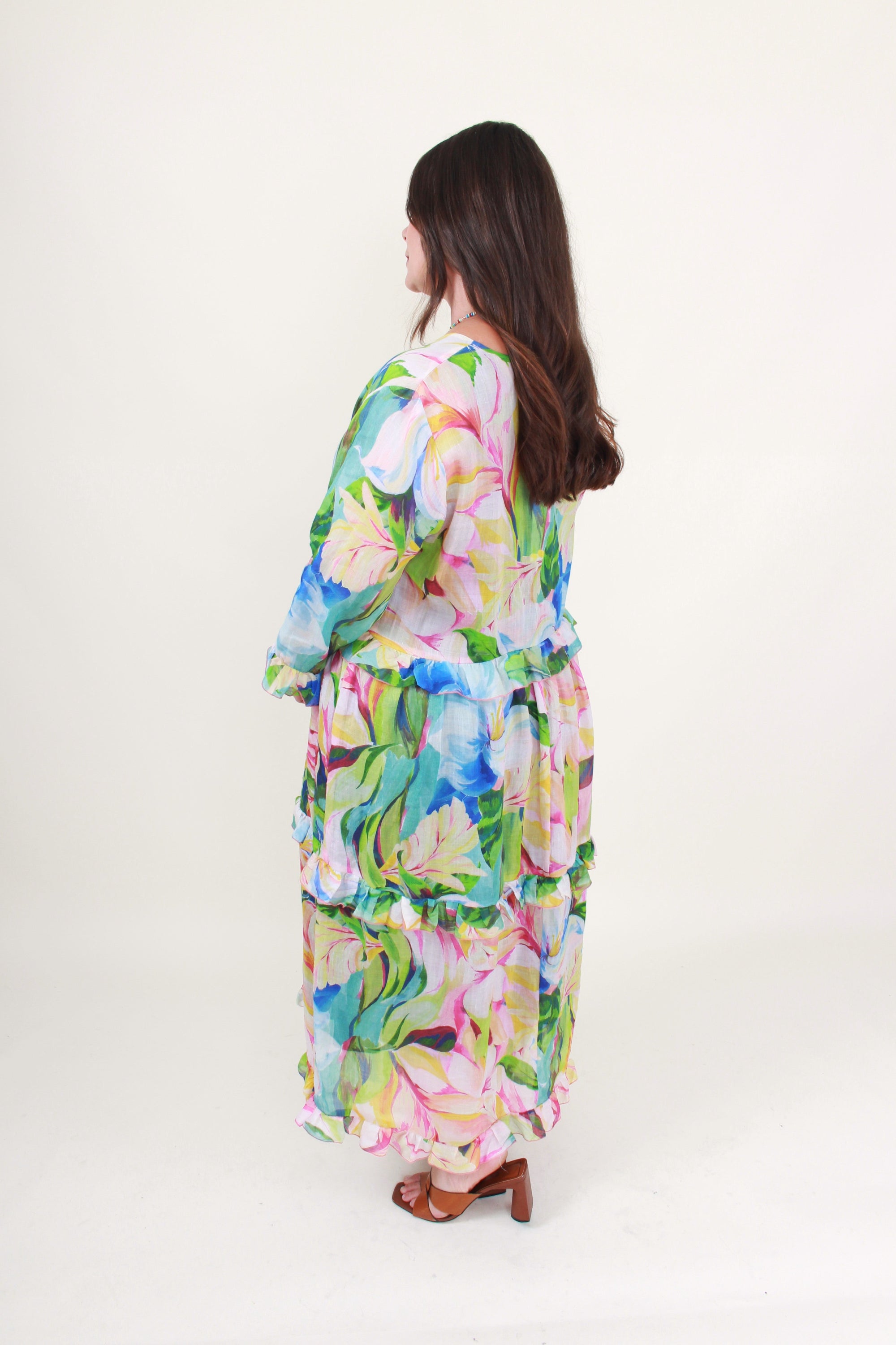 Woman wearing a colorful floral dress on a white background side back view