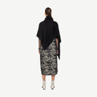 Woman wearing a black top and patterned skirt on a white background back angle