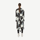 Person wearing a black and white abstract patterned coat on a white background back angle