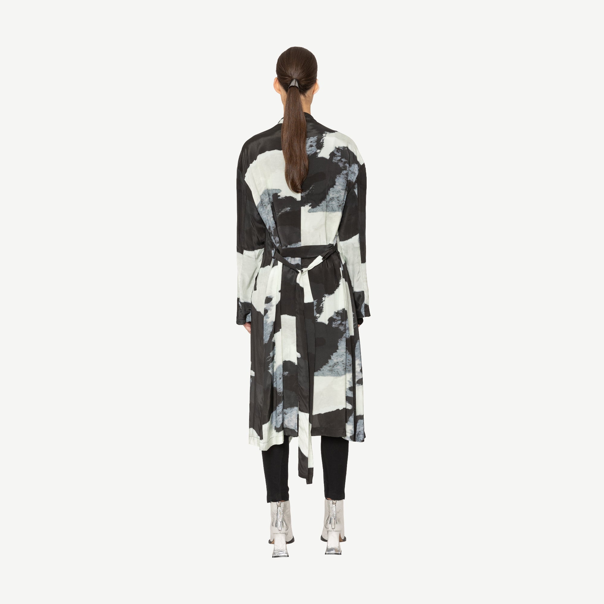 Person wearing a black and white abstract patterned coat on a white background back angle