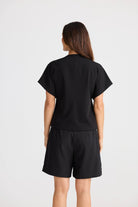 Model wearing black structural top and black shorts on white background back