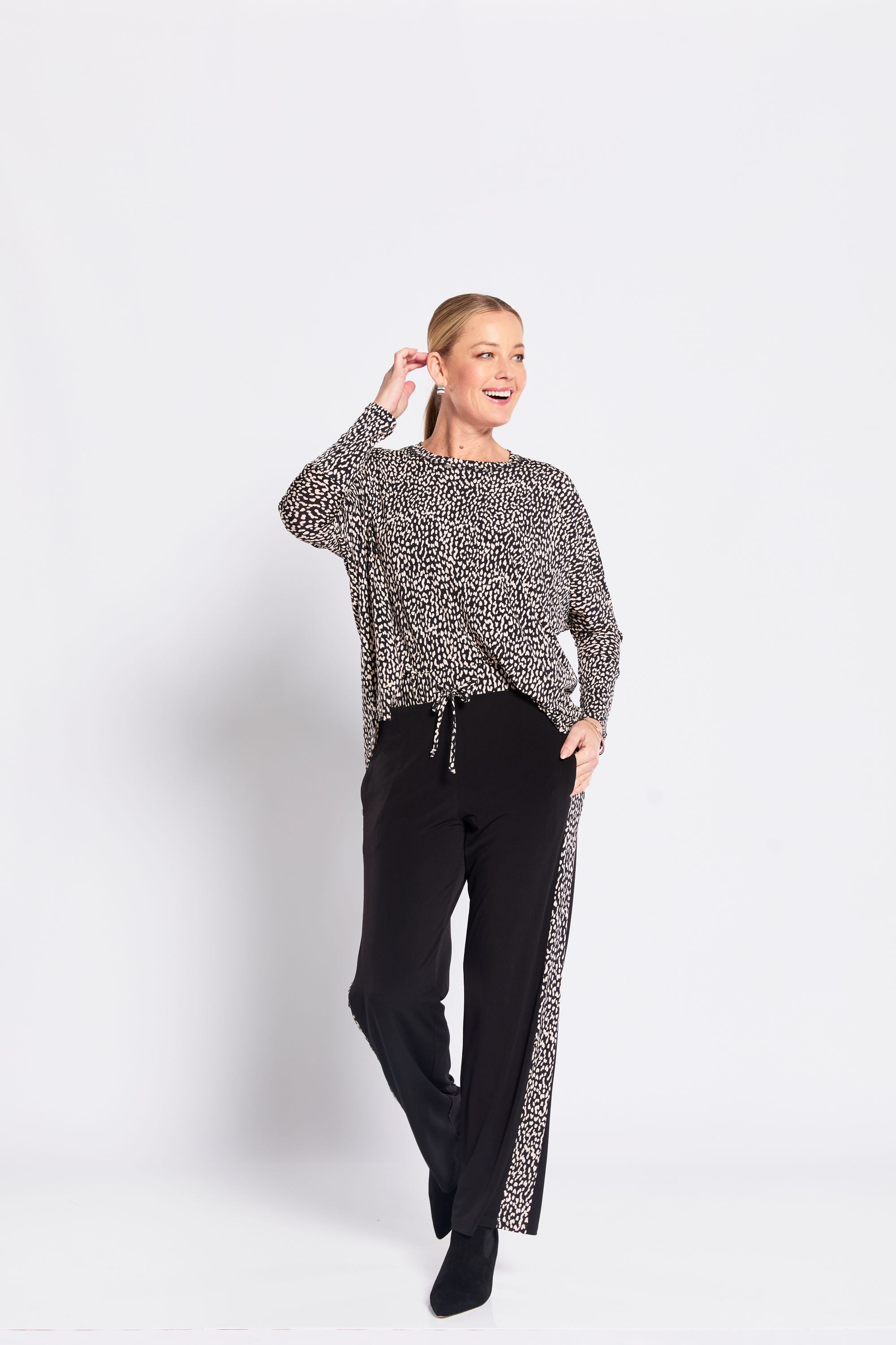 Woman wearing a patterned sweater and black pants on a white background