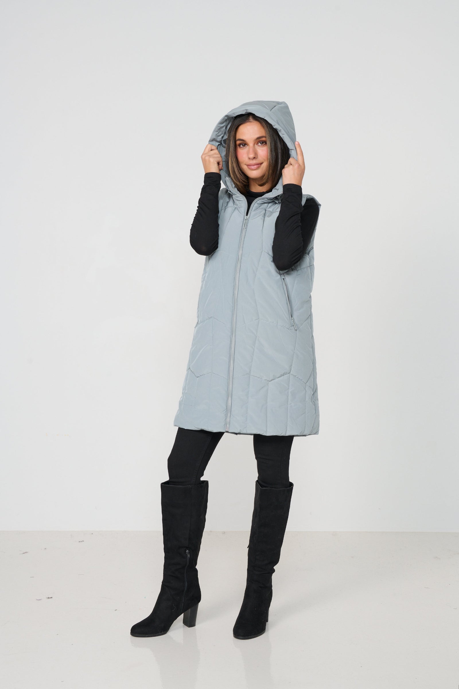 Woman wearing a light blue puffer vest over a black hoodie on a white background