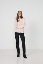 Woman wearing a light pink sweater and black pants with knee-high boots on a white background