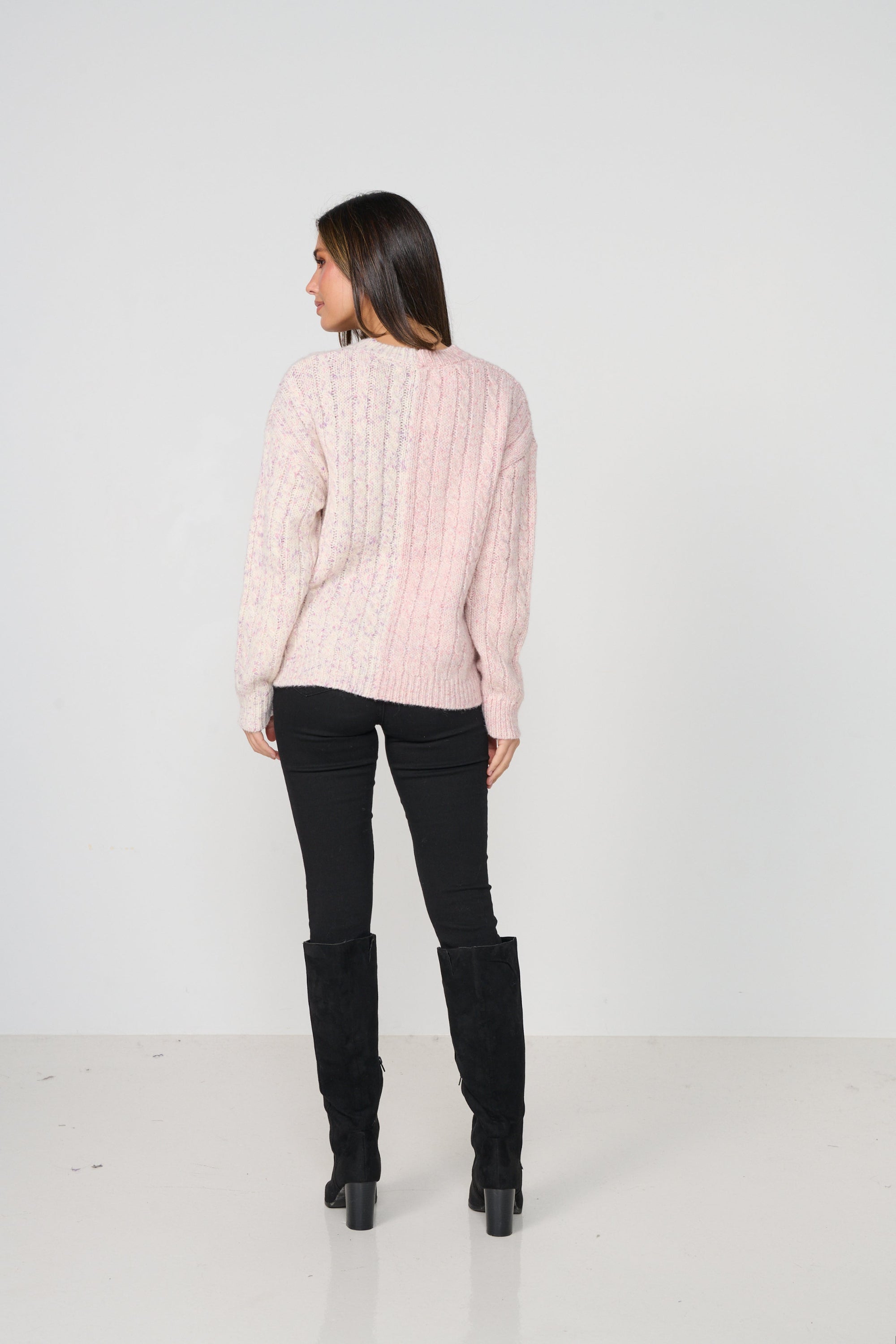 Woman wearing a light pink sweater and black pants on a white background back angle