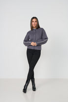Woman wearing a gray cardigan with white trim, black pants, and black boots on a white background