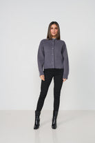 Woman wearing a gray cardigan, black pants, and black boots on a white background