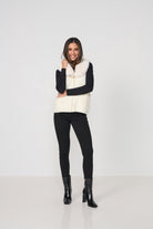 Woman wearing a white puffer vest over a black long-sleeve top, black pants, and black boots on a white background.