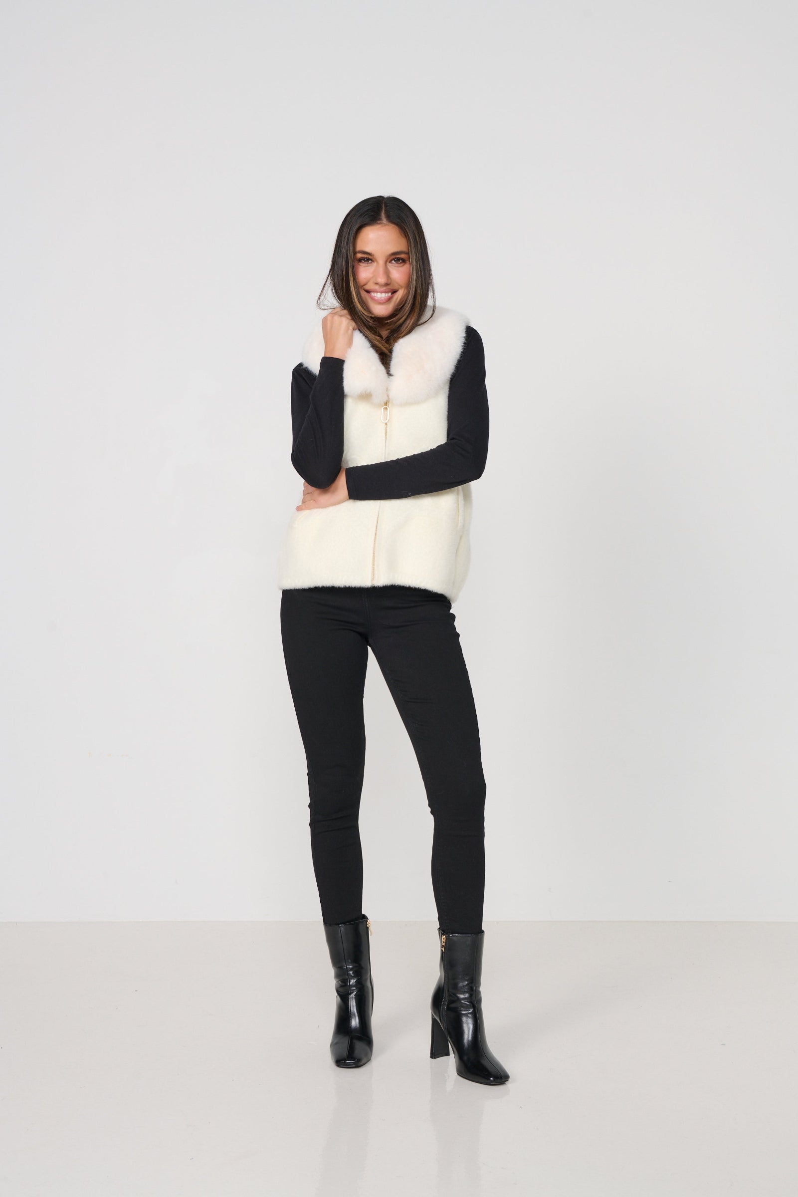 Woman wearing a white puffer vest over a black long-sleeve top, black pants, and black boots on a white background.