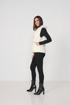 Woman wearing a white vest over a black top and pants on a white background