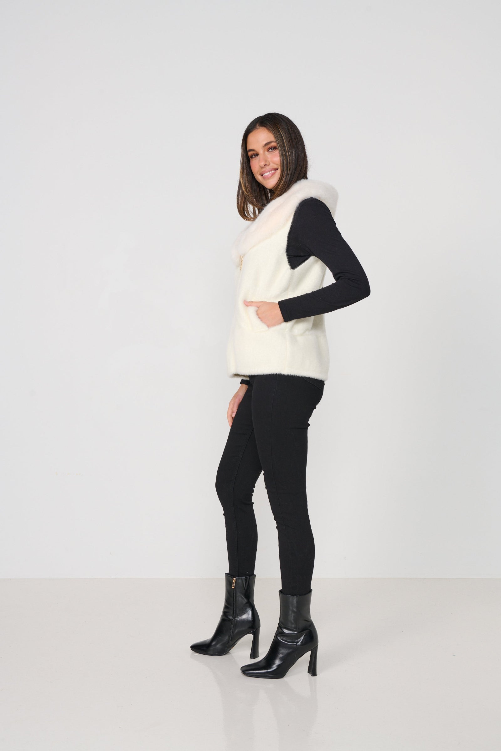 Woman wearing a white vest over a black top and pants on a white background