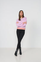 Woman wearing a pink sweater and black pants on a white background