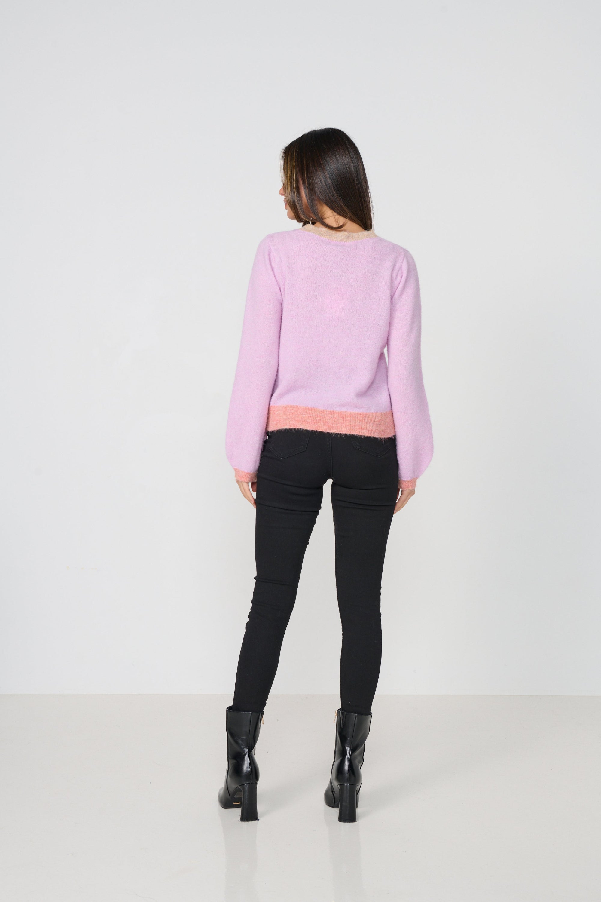 Person wearing a light pink sweater with a white background back angle