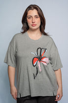 Woman wearing a grey t shirt with flower motif and black pants against a white background.