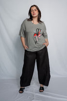 Woman wearing a grey t shirt with flower motif and black pants against a white background.
